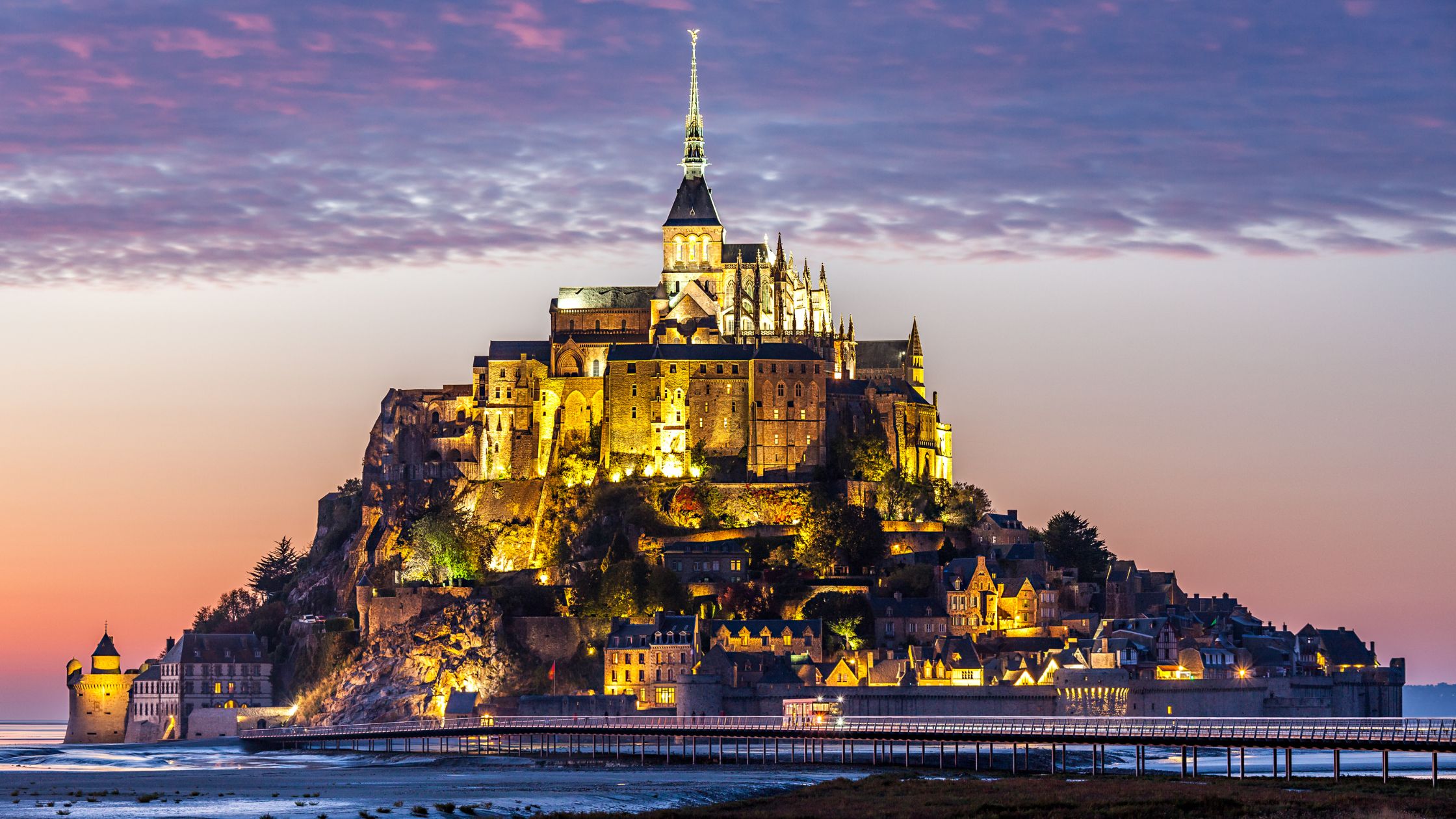 Scenic panoramic view of Mont Saint-Michel abbey surrounded by tidal waters in Normandy France at sunset.